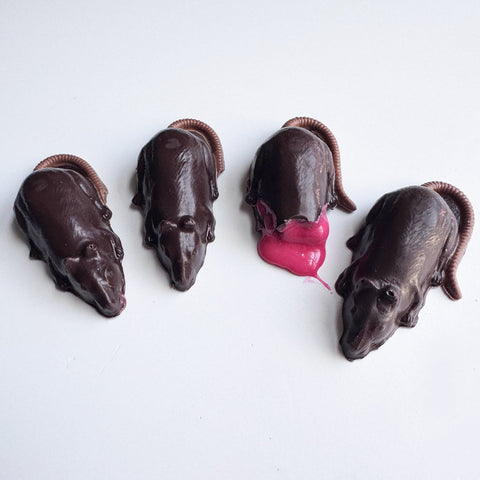 Four chocolate mice or rats sitting on a white back drop. One of the chocolate mice has been bitten and strawberry cream candy filling is oozing out.