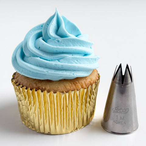 1M piping tip along side a cupcake with light blue buttercream frosting swirl in a gold foil cupcake liner.