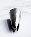 A stainless steel 1M pastry piping tip, resting on it's side a white marble surface.