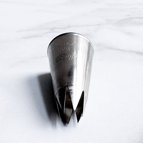 A stainless steel 1M pastry piping tip, resting on it's side a white marble surface.