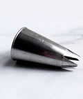 A 1M stainless steel metal piping tip with an open star design, resting on a light gray marble surface.