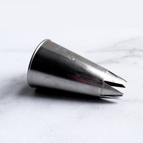 A 1M stainless steel metal piping tip with an open star design, resting on a light gray marble surface.