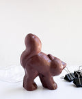 The back side of a 3d chocolate cat next to the clear plastic candy mold and binder clips used to make it. All sitting on a white background.