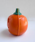 The side profile of an orange chocolate jack-o-lantern pumpkin made with colored Merckens chocolate melts with a green stem, photographed on a plain white background.