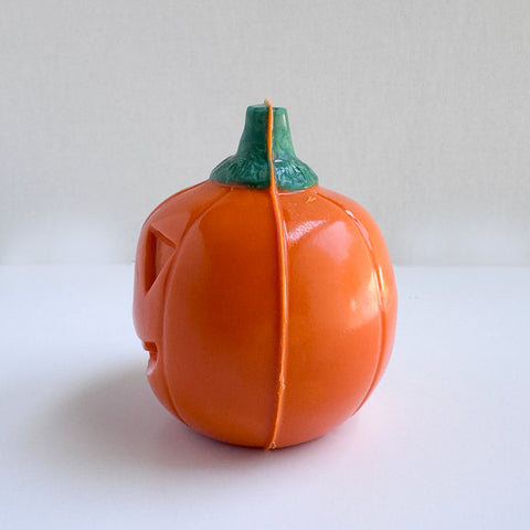 The side profile of an orange chocolate jack-o-lantern pumpkin made with colored Merckens chocolate melts with a green stem, photographed on a plain white background.