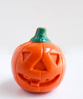 An orange jack-o-lantern pumpkin chocolate with a carved face and a green stem, photographed on a plain white background.