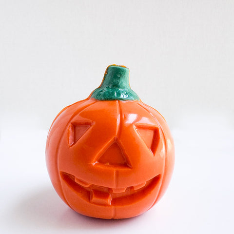 An orange jack-o-lantern pumpkin chocolate with a carved face and a green stem, photographed on a plain white background.