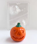 A 3D orange chocolate jack-o-lantern with a green stem, shown in front of a clear plastic candy mold on a white background.