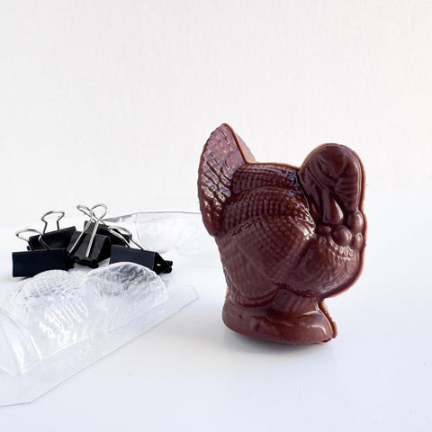 dark chocolate molded turkey with the mold used to make it to the left of it along with the binder clips that were used to secure the mold.