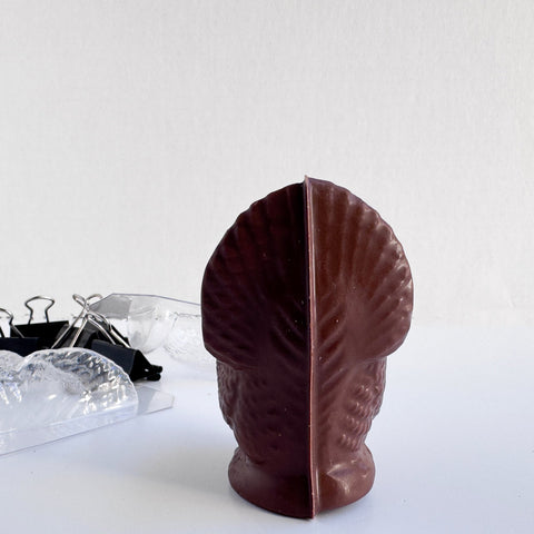 the back side of a 3d dark chocolate molded turkey and the mold used to make it sitting to the left along with the binder clips used to secure the mold when using it.