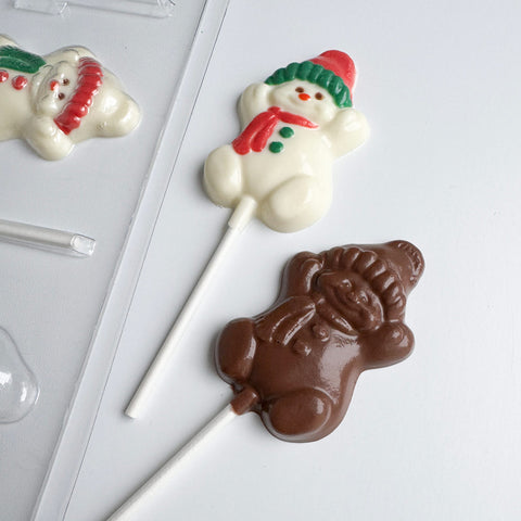 Chocolate lollipops shaped like snowmen along side the plastic mold used to make them.