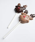 Two chocolate reindeer lollipops on white sticks against a light gray background