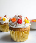 turkey shaped sprinkles in fall colors on a cupcake with white frosting and a gold cupcake liner.