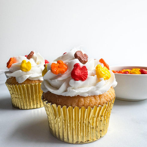 turkey shaped sprinkles in fall colors on a cupcake with white frosting and a gold cupcake liner.