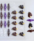 A clear plastic Halloween-themed candy mold with rows of witch and bat shaped cavities, shown alongside several finished molded pieces in dark chocolate and purple, all sitting on a white background.
