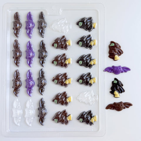 A clear plastic Halloween-themed candy mold with rows of witch and bat shaped cavities, shown alongside several finished molded pieces in dark chocolate and purple, all sitting on a white background.