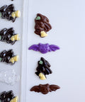 A Halloween chocolate mold and finished chocolate pieces shaped like small witches and bats, shown on a white background.