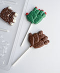 cactus lollipop plastic chocolate mold with chocolate cactus shaped lollipops along side it.