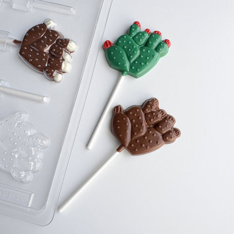 cactus lollipop plastic chocolate mold with chocolate cactus shaped lollipops along side it.