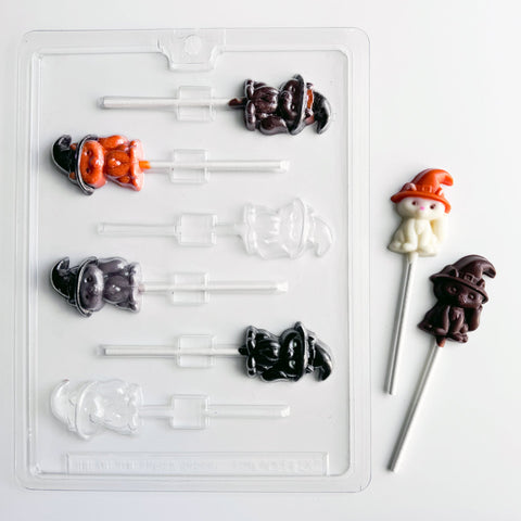 cat with witch or wizard hat shaped chocolate mold for making cat shaped lollipops for Halloween. A clear plastic mold along side two cat shaped lollipops in white chocolate with an orange chocolate hat and the other lollipop made with dark chocolate.