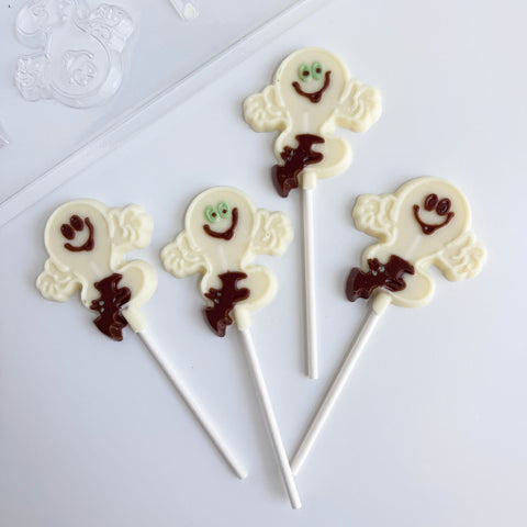Four white chocolate ghost lollipops with dark brown chocolate details and white sticks, arranged on a white background.