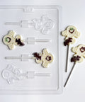 A clear plastic Halloween ghost mold shown with three finished white chocolate ghost lollipops with details decorated in dark chocolate, sitting on a white background.