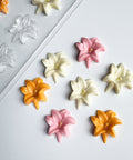 Decorative flower-shaped easter lily candies in orange, pink, and white next to the plastic chocolate mold for making them.