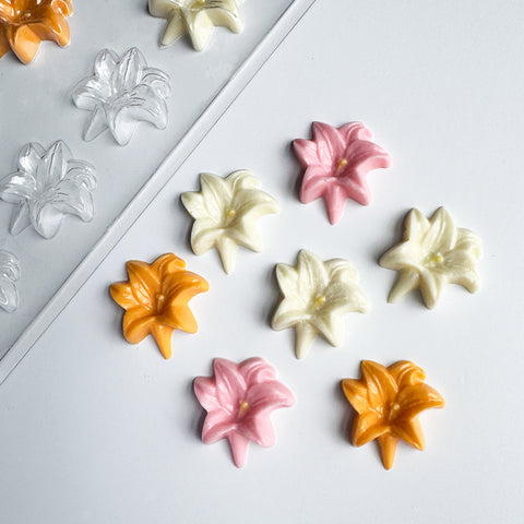 Decorative flower-shaped easter lily candies in orange, pink, and white next to the plastic chocolate mold for making them.