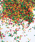 Multicolor round ball shaped nonpareil sprinkles in red, green, yellow, and orange scattered on a white background, with a larger pile concentrated toward the top right.