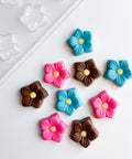 Colorful flower-shaped candies on a white surface with a candy mold in the background.