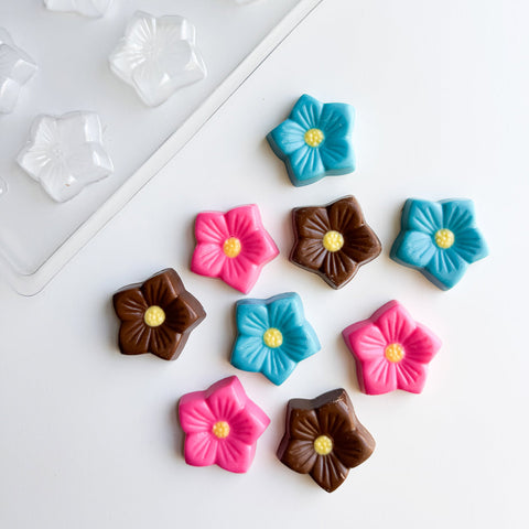 Colorful flower-shaped candies on a white surface with a candy mold in the background.