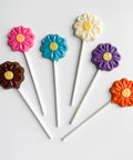 Colorful flower-shaped lollipops on sticks against a white background