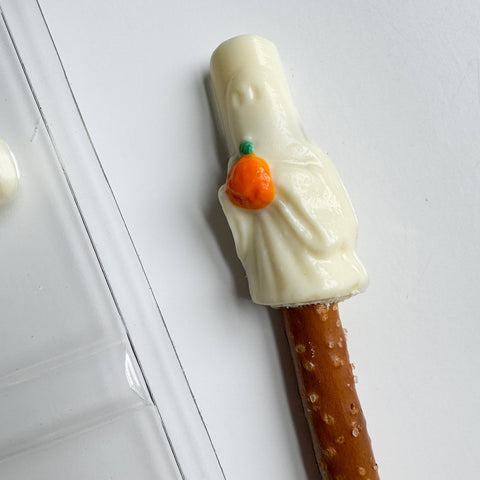 Pretzel rod with white chocolate ghost holding an orange pumpkin.