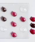 human heart shaped chocolates made with red and dark chocolate with gray accents next to human heart plastic chocolate mold photographed on a white back drop.
