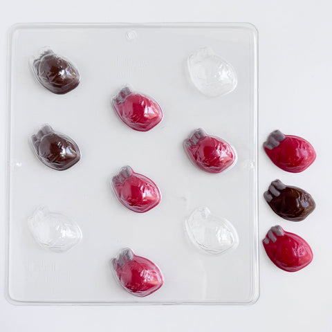 human heart shaped chocolates made with red and dark chocolate with gray accents next to human heart plastic chocolate mold photographed on a white back drop.