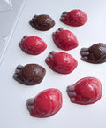 Nine glossy, anatomically shaped chocolate hearts in red and dark brown, arranged on a clean white surface.