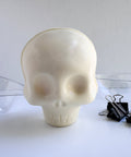 a white chocolate skull along side the clear plastic mold and binder clips used to make it.