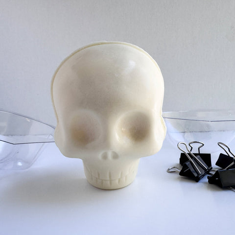 a white chocolate skull along side the clear plastic mold and binder clips used to make it.