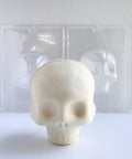 a white chocolate 3d skull in front of two plastic chocolate molds that come as a set to make the skull