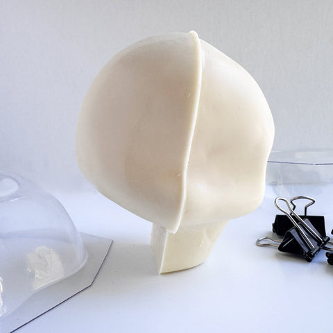 the side view of a white chocolate skull next to the chocolate molds and binder clips used to make it.