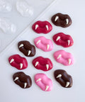 Twelve chocolate lips with fangs pieces along side the plastic candy mold used to make them. Finished chocolate pieces are shown in an assortment of red, pink, and dark chocolate with white chocolate fangs