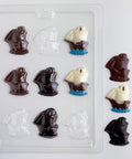 a clear plastic candy mold for making mayflower shaped chocolates. Shown along side finished mayflower chocolates made from milk chocolate, dark chocolate, and one that is made with white chocolate sails, blue chocolate water at the base, and a milk chocolate boat.