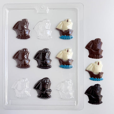 a clear plastic candy mold for making mayflower shaped chocolates. Shown along side finished mayflower chocolates made from milk chocolate, dark chocolate, and one that is made with white chocolate sails, blue chocolate water at the base, and a milk chocolate boat.