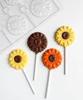 Sunflower-shaped lollipops on sticks with a plastic candy mold in the background