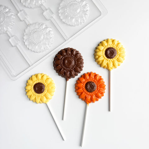 Sunflower-shaped lollipops on sticks with a plastic candy mold in the background