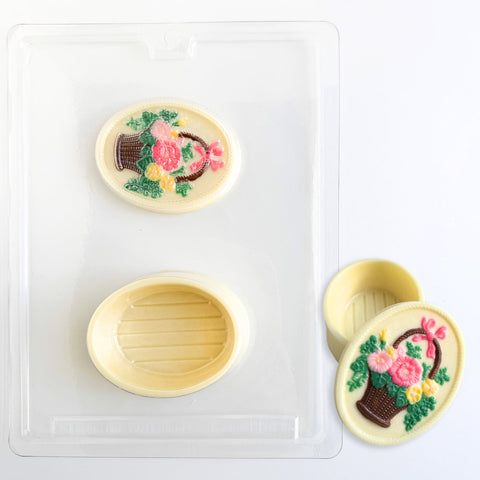 oval box made of chocolate  with a flower and basket design made using the pour box mold shown next to it