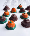 Clear plastic chocolate mold shaped like pumpkins, featuring finished orange pumpkin chocolates with green stems and green leafy bases, and others made from just solid dark chocolate.