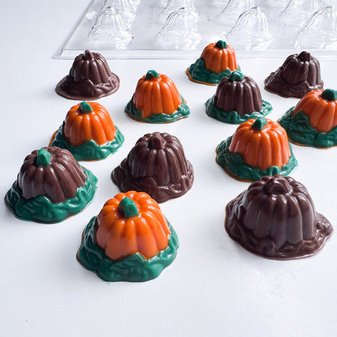 Clear plastic chocolate mold shaped like pumpkins, featuring finished orange pumpkin chocolates with green stems and green leafy bases, and others made from just solid dark chocolate.