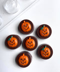 Six chocolate covered oreo cookies molded with a sandwich cookie mold with orange pumpkin faces and green leaf accents, arranged on a white surface next to the chocolate mold used to make them