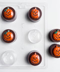 Six Halloween-themed chocolate covered sandwich cookies with jack-o'-lantern faces in orange and brown, shown with the sandwich cookie plastic candy mold used to make them.